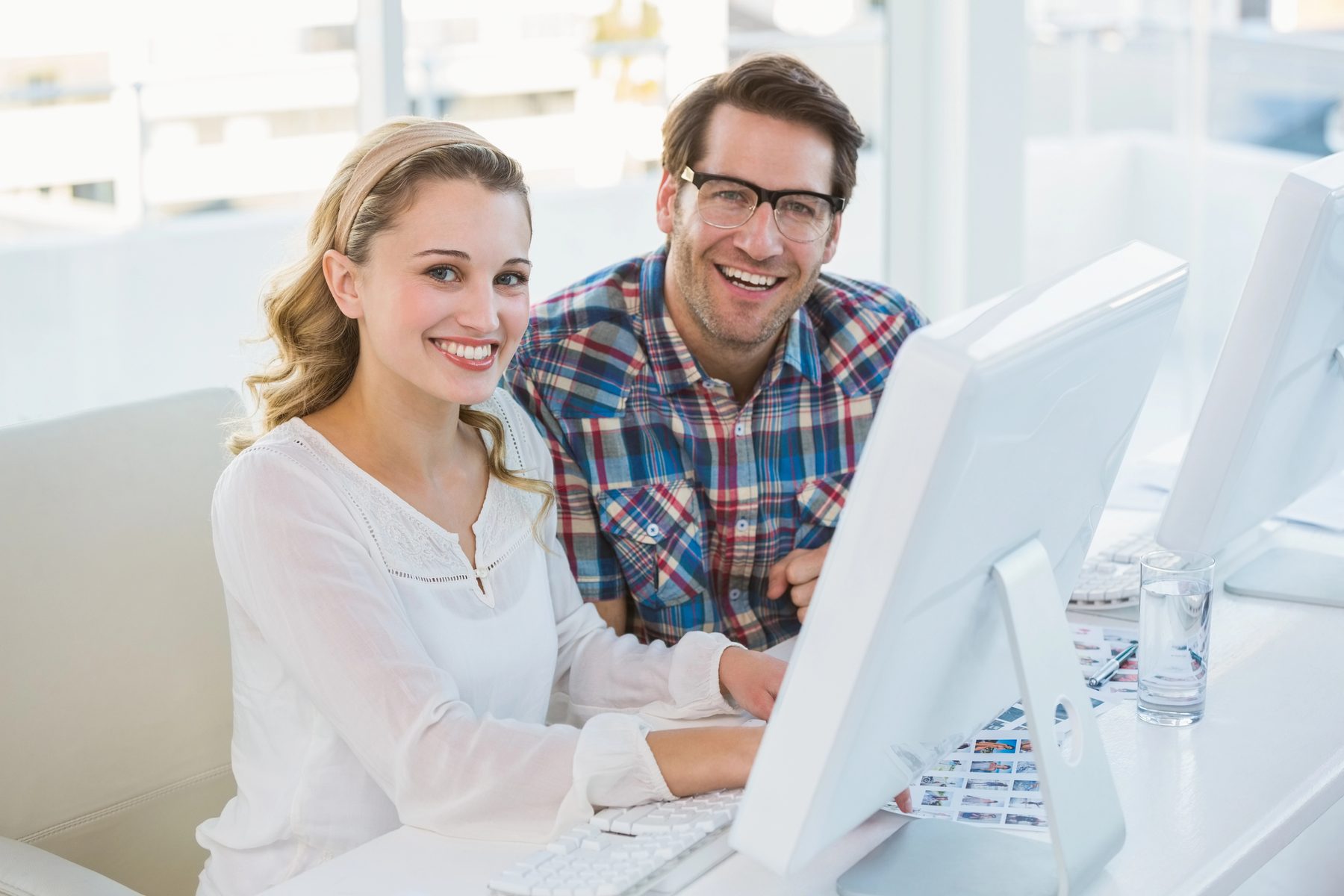 Two coworkers smiling at a computer in a bright office